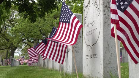 Close-up-side-view-of-gravestones-in-a-cemetery-of-civil-war-soldiers-remains-on-Memorial-day-with-American-flags-flapping-in-the-wind