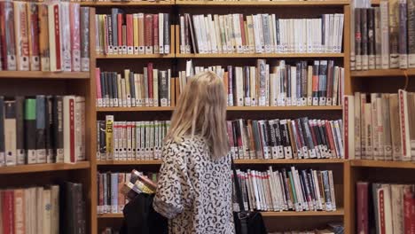 Young-girl-walking-between-bookshelves-in-library,-dolly-shot-with-books-all-around