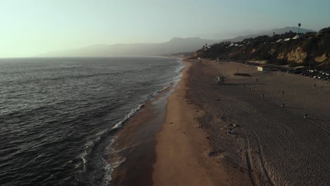 Eine-Luftaufnahme-Mit-Blick-Auf-Einen-Strand,-Während-Die-Wellen-Am-Abend-Bei-Sonnenuntergang-Auf-Den-Strand-In-Der-Nähe-Von-Point-Dume-In-Malibu-In-Kalifornien-Rollen