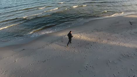 Aerial-Tracking-Shot-of-a-Man-Running-By-The-Waves-on-The-Beach-In-The-Evening-Sunset-in-Ystad-South-Sweden-Skåne-in-The-Summer