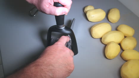 Slow-motion-of-man's-hands-sharpening-a-kitchen-knife-on-a-sharpener,-peeled-potatoes-on-kitchen-top