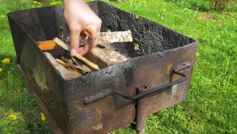 Young-man-laying-down-wood-log-and-prepares-rusty-grill-for-baking-and-BBQ,-medium-close-up-shot