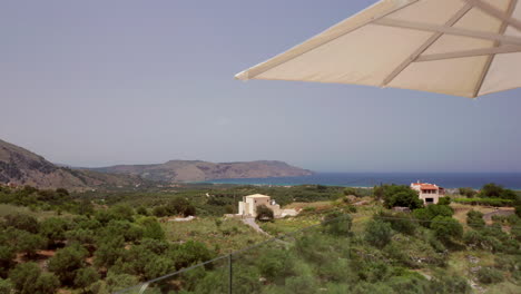 Aerial-Fly-Through-of-Luxury-Greek-Villa-Patio---Loungers-revealing-Coastline-in-the-Distance-in-Crete,-Greece