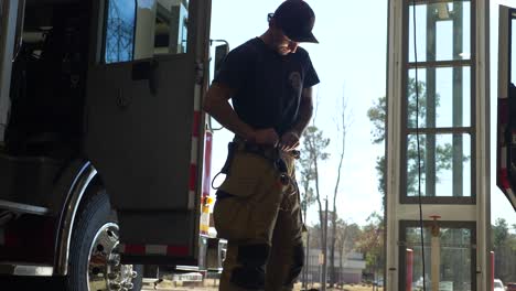 Firefighter-puts-on-protective-firefighting-pants-as-he-prepares-to-respond-to-an-emergency