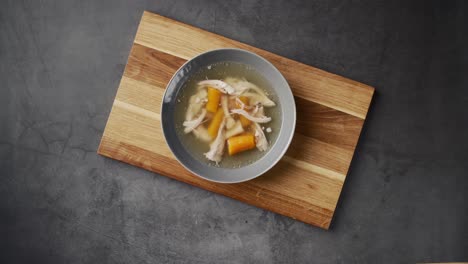 Top-view-of-serving-fresh-hot-healthy-paleo-chicken-broth-soup-to-wooden-board-on-concrete-background