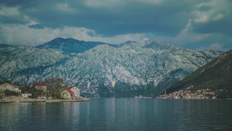 Kineographie-Eines-Alten-Dorfes-In-Der-Lagune-In-Der-Nähe-Von-Kotor-In-Montenegro-Mit-Bergen-Im-Hintergrund-Und-Sanft-Fließendem-Wasser