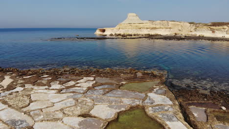 An-aerial-drone-shot-flying-over-the-Salt-Pans,-rocks-and-crystal-blue-water-of-Gozo-Island-in-Malta
