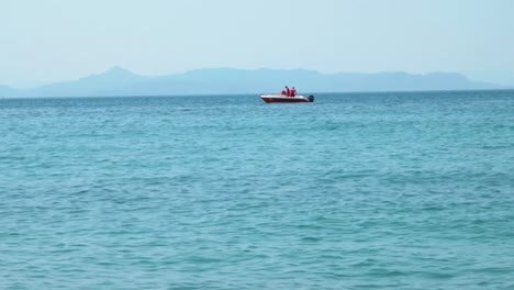 Small-Motor-Boat-on-light-blue-sea-with-mountains-in-the-background