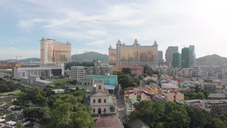 Rising-drone-reveal-shot-of-Taipa-skyline-in-Macau-with-park-and-church-in-foreground-and-casino-hotel-in-background