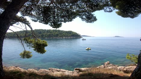 Beautiful,-hot,-sunny-day-view-over-sea-from-the-shaded-pine-treetops-with-rocky-coastline-beneath-your-feet