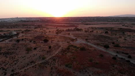Drone-landing-in-desert-during-sunset-with-car-passing-by-in-the-background-In-Albufeira,-Portugal