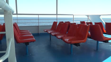 Push-in-to-red-outdoor-ferry-seats-in-between-railings-with-open-sea-in-distance