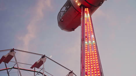 Carnival-ride-stopped-in-the-sky-with-ferris-wheel-and-moon-in-the-background,-Slow-Motion
