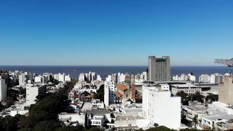 Aerial-view-of-the-city-Montevideo-Uruguay,-with-buildings,-a-construction-crane,-the-sea-and-the-clear-sky-in-the-background