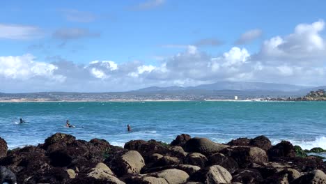 Surfer-In-Neoprenanzügen-Warten-Darauf,-Eine-Welle-Zu-Erwischen,-Während-Ein-Vater-Und-Sein-Sohn-Die-Gezeitentümpel-Des-Ozeans-Im-Monterey-County-Erkunden
