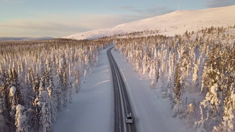 Cars-driving-on-a-empty-road-surrounded-by-snowy-trees-in-Lapland-Finland