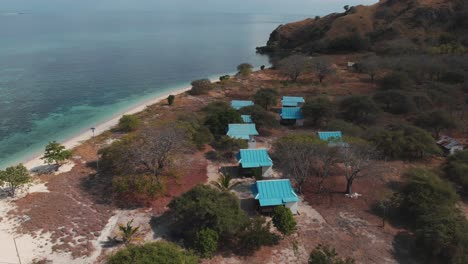 Aerial-drone-shot-of-the-island-house's-roofs-surrounded-of-amazing-turquoise-ocean-water-with-coral-reefs-and-nature
