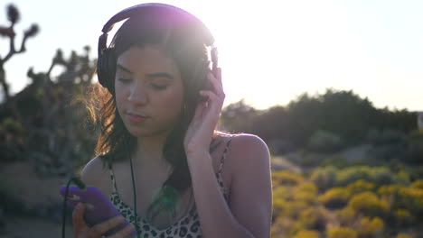 A-beautiful-young-hispanic-woman-holding-a-smartphone-listening-to-sad-or-serious-music-on-headphones-outdoors-in-sunlight-lens-flares-SLOW-MOTION