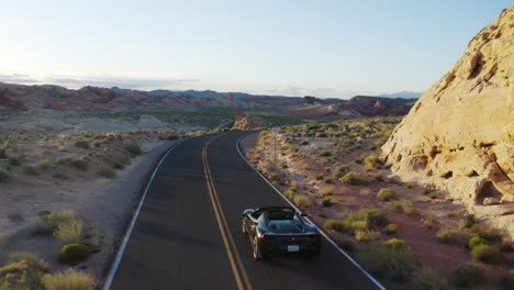 Black-Ferrari-driving-along-a-twisting-road-in-the-Valley-of-Fire,-Nevada,-USA,-at-sunset