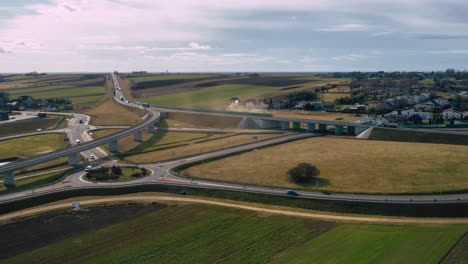 Aerial-wide-angle-fly-by-shot-of-the-traffic-on-a-highway-ring-road-roundabout-on-a-bright-sunny-afternoon