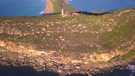 Aufschlussreiche-Luftaufnahme-Des-Leuchtturms-Barrenjoey-Head-Auf-Der-Spitze-Des-Sandsteinfelsens-Der-Landzunge-Bei-Sonnenaufgang-Und-Sonnenuntergang,-Der-über-Palm-Beach-Und-Die-Kaputte-Bucht-An-Der-Küste-Von-Sydney-Im-Hintergrund-Fliegt
