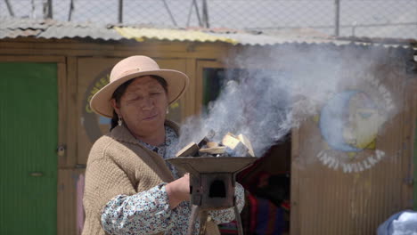 Bolivian-woman-holds-portable-fire-stove-outside-her-home-in-La-Paz,-Bolivia
