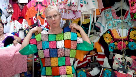 Mature-woman-holds-up-colorful-mexican-crocheted-blouse-and-asks,-do-you-like-it-and-smiles-in-Merida,-Mexico