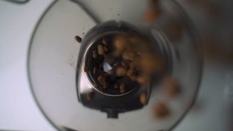 Slow-motion-up-close-overhead-view-of-fresh,-brown-coffee-beans-being-scattered-and-poured-into-fancy-electric-grinder-for-morning-coffee