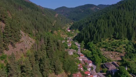 Flying-backwards-over-a-small-town-in-the-mountains-surrounded-by-green-hills-and-trees