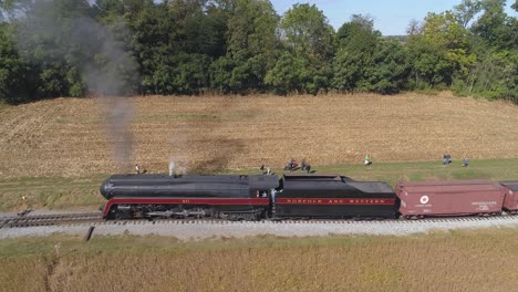 Aerial-View-of-a-Antique-Steam-Engine-Pulling-away-from-Station-with-Freight-Cars-Through-Amish-Farm-Lands-on-a-Sunny-Autumn-Day-With-a-Pull-Away-View-as-Seen-by-a-Drone