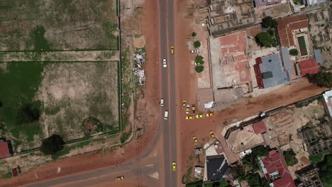 Aerial-bird's-eye-view-tracking-a-white-van-on-Kololi-Road-in-Serrekunda-Africa-with-red-dusty-roads
