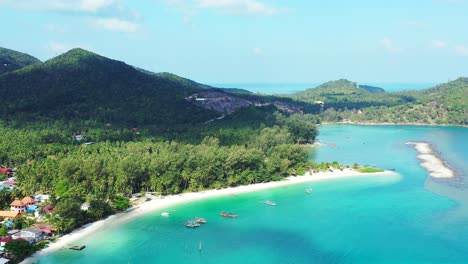 Paradise-beach-with-white-sand-washed-by-calm-turquoise-lagoon-on-tropical-island-with-vacation-resorts-into-green-forest,-Thailand