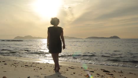 Silhouette-of-young-woman-walking-at-a-beach-at-sunset-with-Cies-island-at-the-background