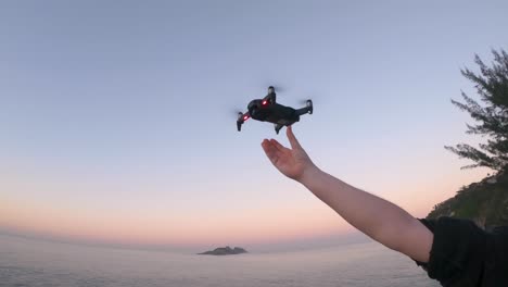 Small-drone-returning-home-and-steadily-hand-landing-after-a-flight-with-a-first-hesitation-and-calm-landing-with-a-cliff-and-island-in-the-background-against-a-blue-sky