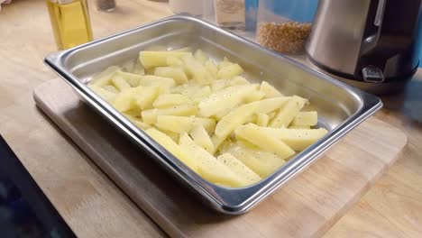 Slow-Motion-Slider-Shot-of-Seasoning-Homemade-Oven-Fries-in-a-Metal-Baking-Tray-prior-to-Cooking-in-the-Kitchen