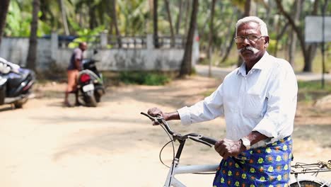 Scene-of-serious-Indian-elderly-with-bike-that-stops-and-looks-at-camera