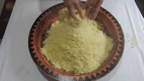 Woman-rolling-hot-semolina-of-couscous-between-her-fingers-in-a-wooden-dish-at-home-after-steaming-it