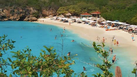 Strand-Von-Grote-Knip-Auf-Curaçao-–-Touristen-Genießen-Das-Strahlend-Blaue-Meerwasser,-Während-Andere-Sich-Bei-Sonnigem-Wetter-Am-Ufer-Sonnen-–-Panoramaaufnahme