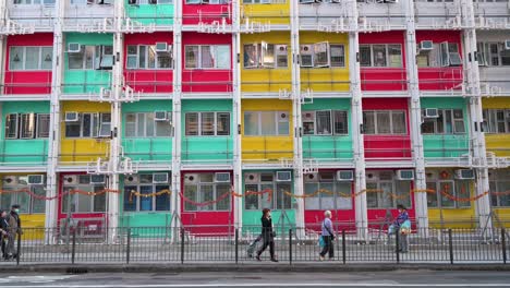 Fußgänger-Werden-Gesehen,-Wie-Sie-An-Einer-Farbenfrohen-Fassade-Eines-Sozialwohnungsgebäudes-In-Hongkong-Vorbeigehen