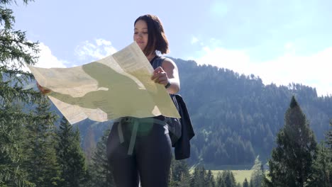 Young-female-hiker-with-backpack-spreads-foldable-map-in-sunny-mountain-landscape-and-looks-for-the-right-way-for-her-tour-through-the-mountains