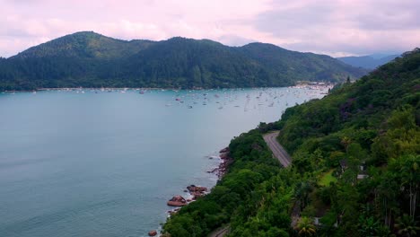 Aerial:-drone-shot-in-brazil-santa-rita-beach-ubatuba-with-view-to-yacht-park-sailboats-in-ubatuba-on-the-road-that-passes-near-the-sea-and-the-jungle-during-sunset-sao-paulo-san-pablo-litoral-north