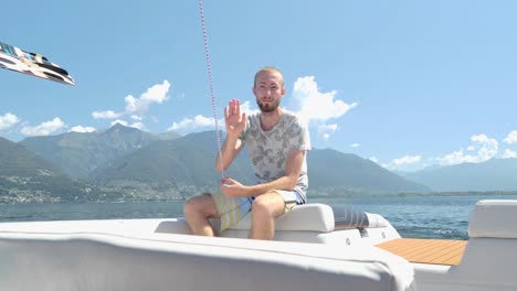 Slow-motion-man-sitting-back-boat-waving-at-camera,-on-a-beautiful-sunny-clear-sky-in-Italy