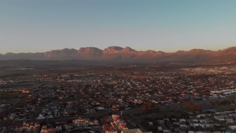 Drone-footage-of-a-city-with-a-mountain-range-in-the-background-at-dusk