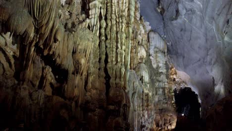 Tourists-looking-at-giant-stalagmite-and-stalactite-calcium-deposit-formations-in-the-cavern,-Walking-tilt-up-shot