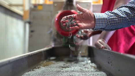 cinematic-shot-of-white-male-hand-picking-up-and-dropping-grey-recycled-plastic-pellets-in-a-recycling-plant
