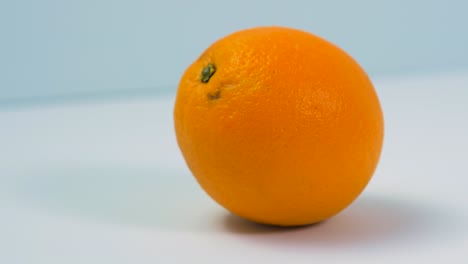 Frische,-Große,-Saftige-Orange-Dreht-Sich-Langsam-Auf-Hellblauem-Hintergrund,-Gesundes-Ernährungskonzept,-Extreme-Nahaufnahme,-Kamera-Dreht-Sich-Nach-Links
