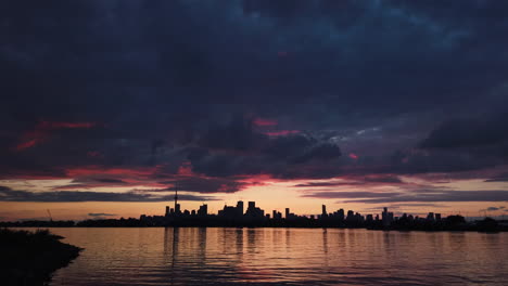 Kippen-Sie-Von-Einem-Bedrohlichen,-Mit-Rosa-Wolken-Gefärbten-Himmel-Hinab-Zu-Einem-Atemberaubenden-Lake-Ontario-Und-Der-Skyline-Von-Toronto,-Die-Sich-In-Der-Dämmerung-Abzeichnet