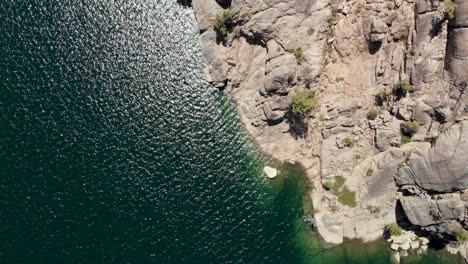 Top-down-aerial-shot-along-the-shores-of-a-blue-high-Sierra-lake-in-California