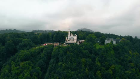Aerial-view-over-forest-towards-the-Chateau-Gutsch-castle-and-luxury-hotel,-dark,-gloomy,-summer-day,-in-Luzern,-Switzerland---rising,-drone-shot