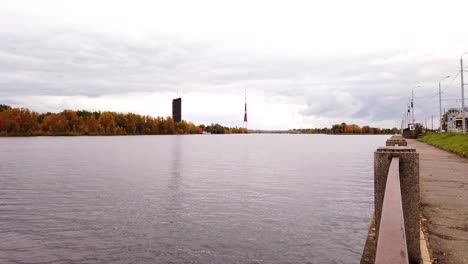 Television-tower-of-Riga-from-Dauguva-river-shore-with-calm-and-still-water-in-cloudy-autumn-day